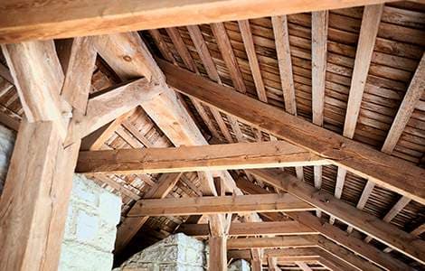 Charpente traditionnelle en bois massif avec poutres apparentes et chevrons sous un toit rustique.