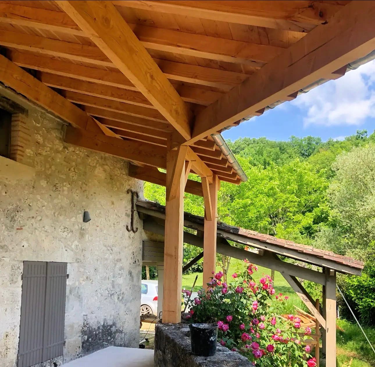 Auvent en bois massif sur une maison en pierre avec vue sur la forêt.
