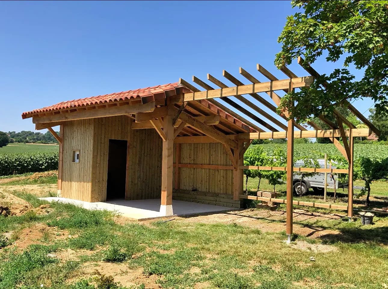 Abri en bois en construction avec toit de tuiles rouges sous un ciel bleu.